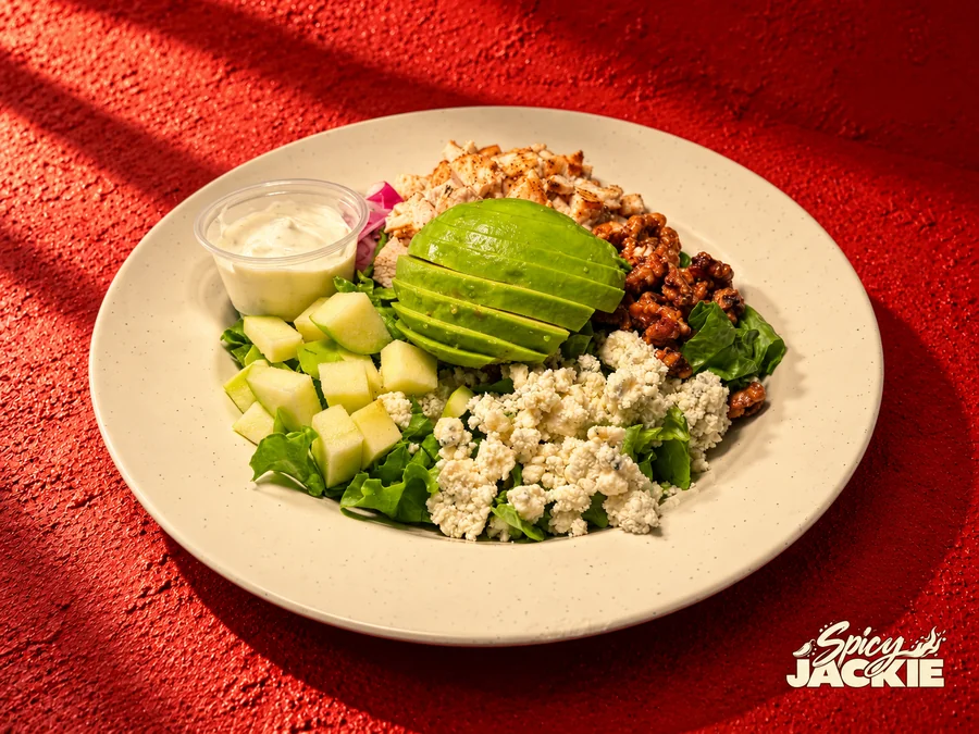 Chicken and avocado salad with apple slices, walnuts, crumbled cheese, and a cup of dressing