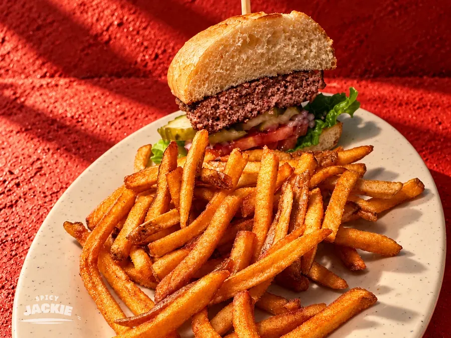 Burger with lettuce and tomato on a white plate piled with fries