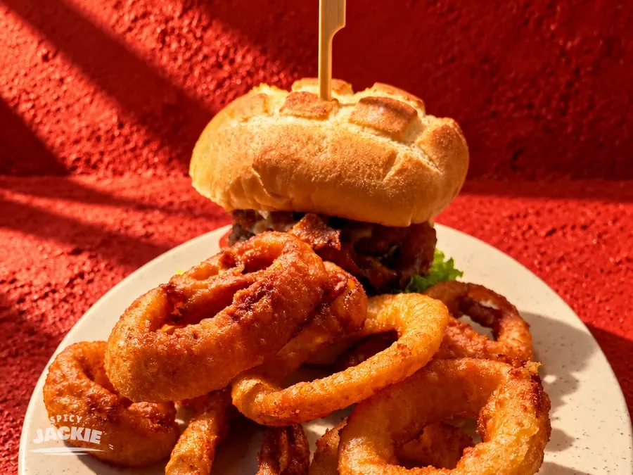 Burger and golden onion rings together on a white plate