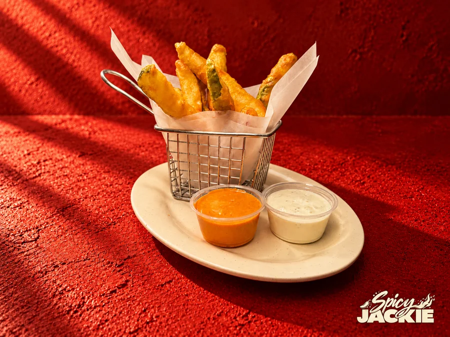 A wire basket of battered pickle spears with orange and white dipping sauces
