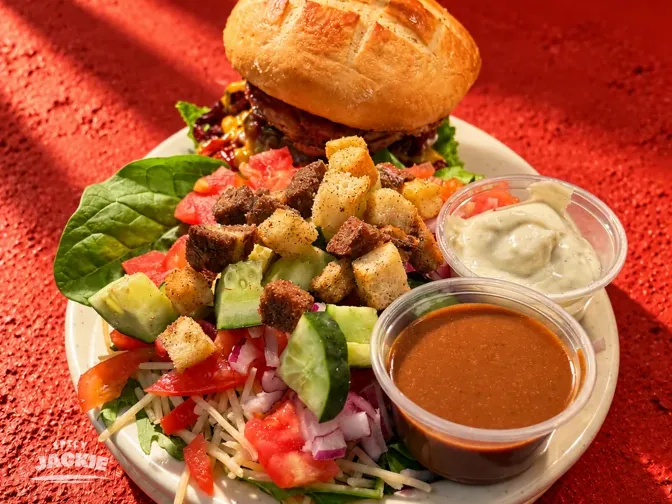 Burger served with a mixed green salad and small cups of dressing