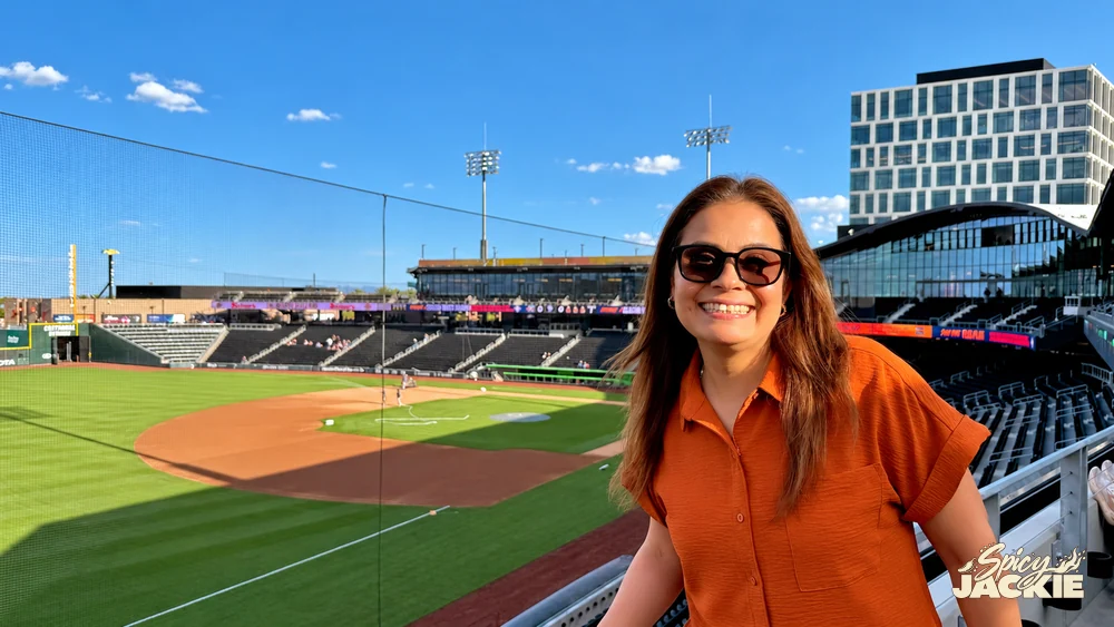 Jackie in sunglasses beside a baseball field on a sunny day