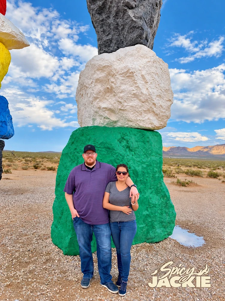 Jackie and a companion beside a stack of brightly painted rocks in the desert