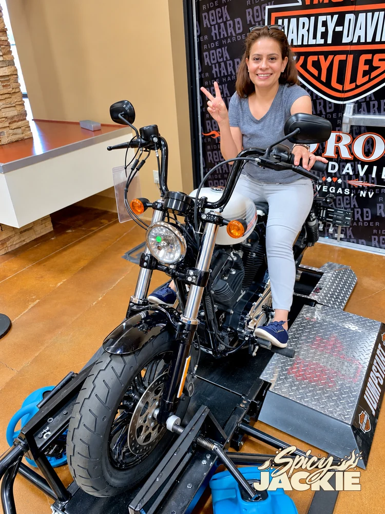 Jackie sitting on a motorcycle and making a peace sign indoors