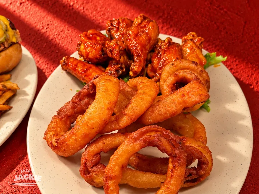 Sauced chicken wings and golden onion rings on a white plate
