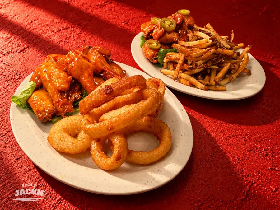 Sauced chicken wings and onion rings, with a second plate of wings and fries behind