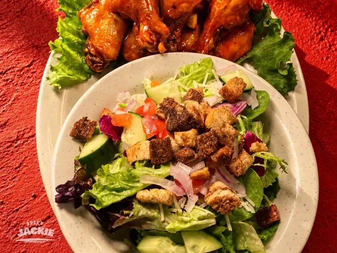 Sauced chicken wings and a green salad on white plates