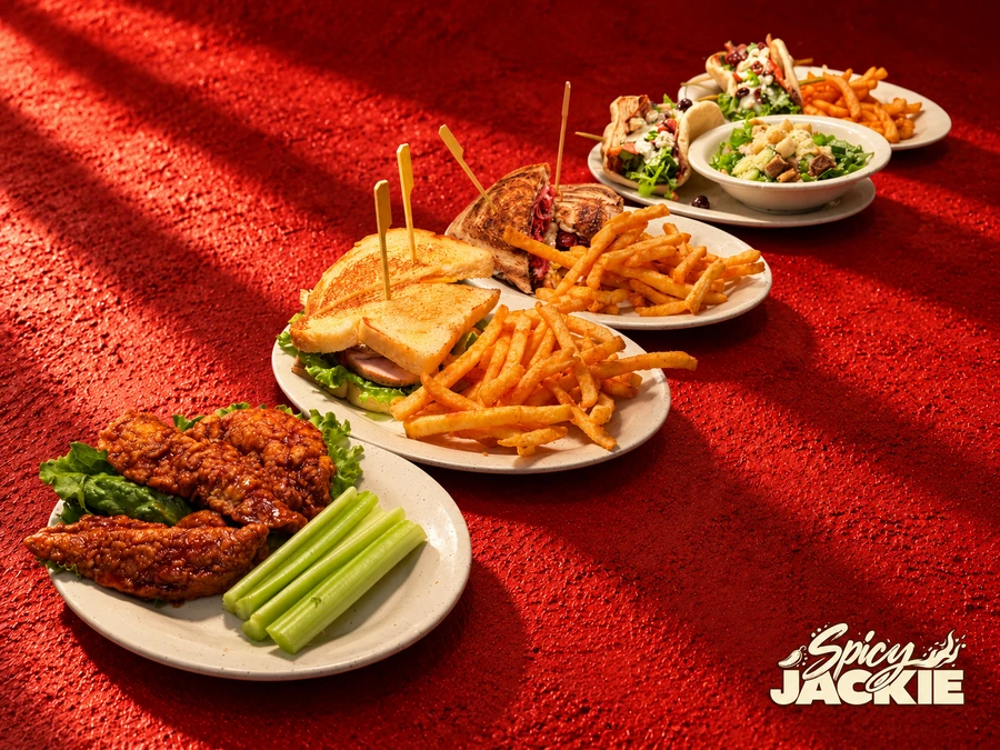 A diagonal lineup of wings with celery, toasted sandwiches with fries, and pita sandwiches with salad and fries against a textured red background